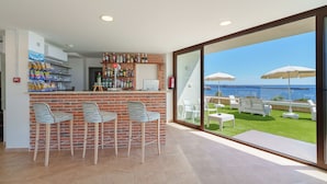 Eine Bar mit Backsteinwand, Barhocker und Meerblick durch große Fenster.