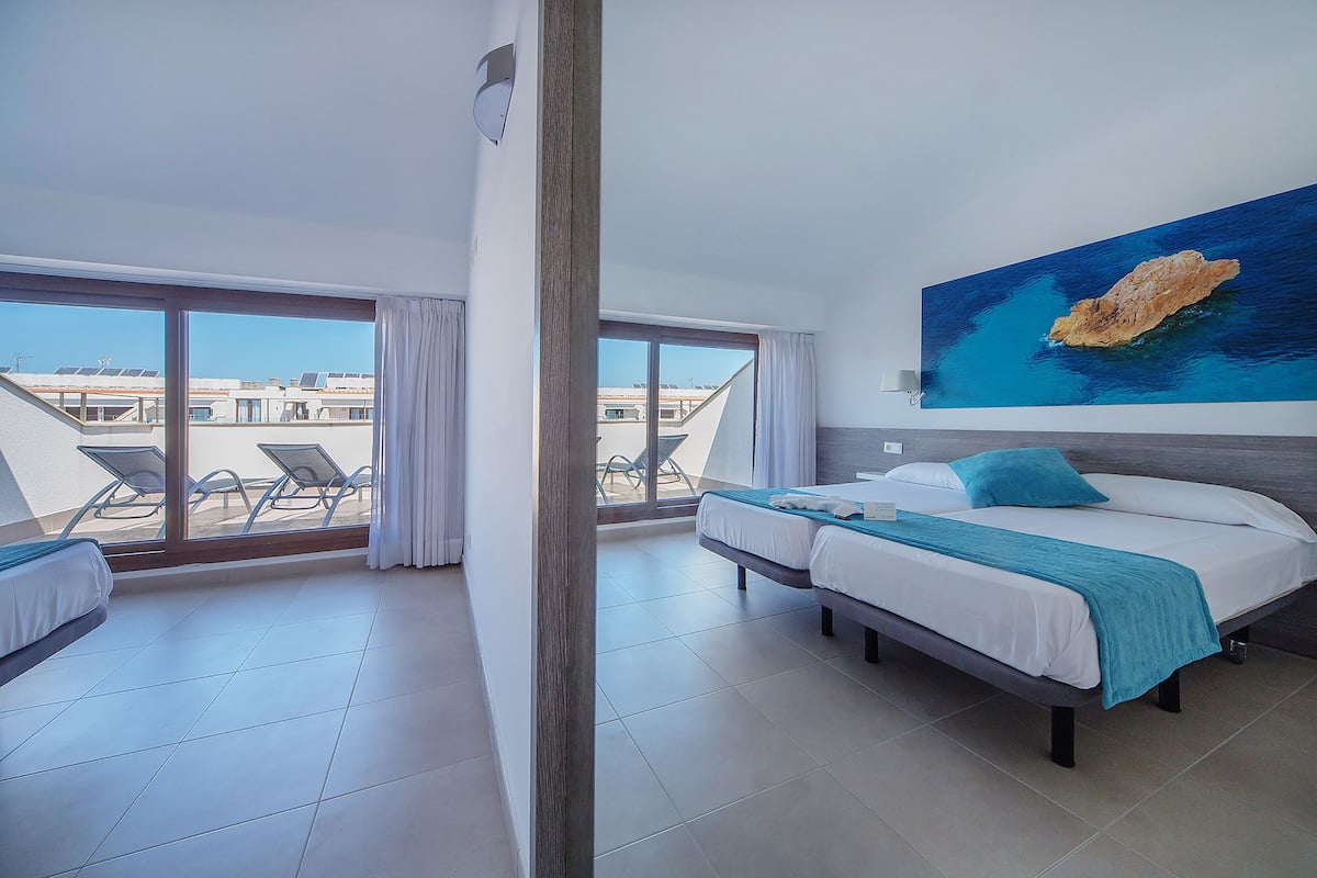 A hotel room with a balcony, a bed, a desk, and a large window.