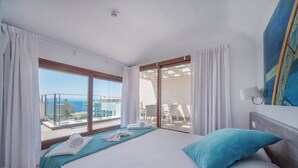 Ein Hotelzimmer mit einem großen Bett, Meerblick und einem Balkon mit Sitzgelegenheit.