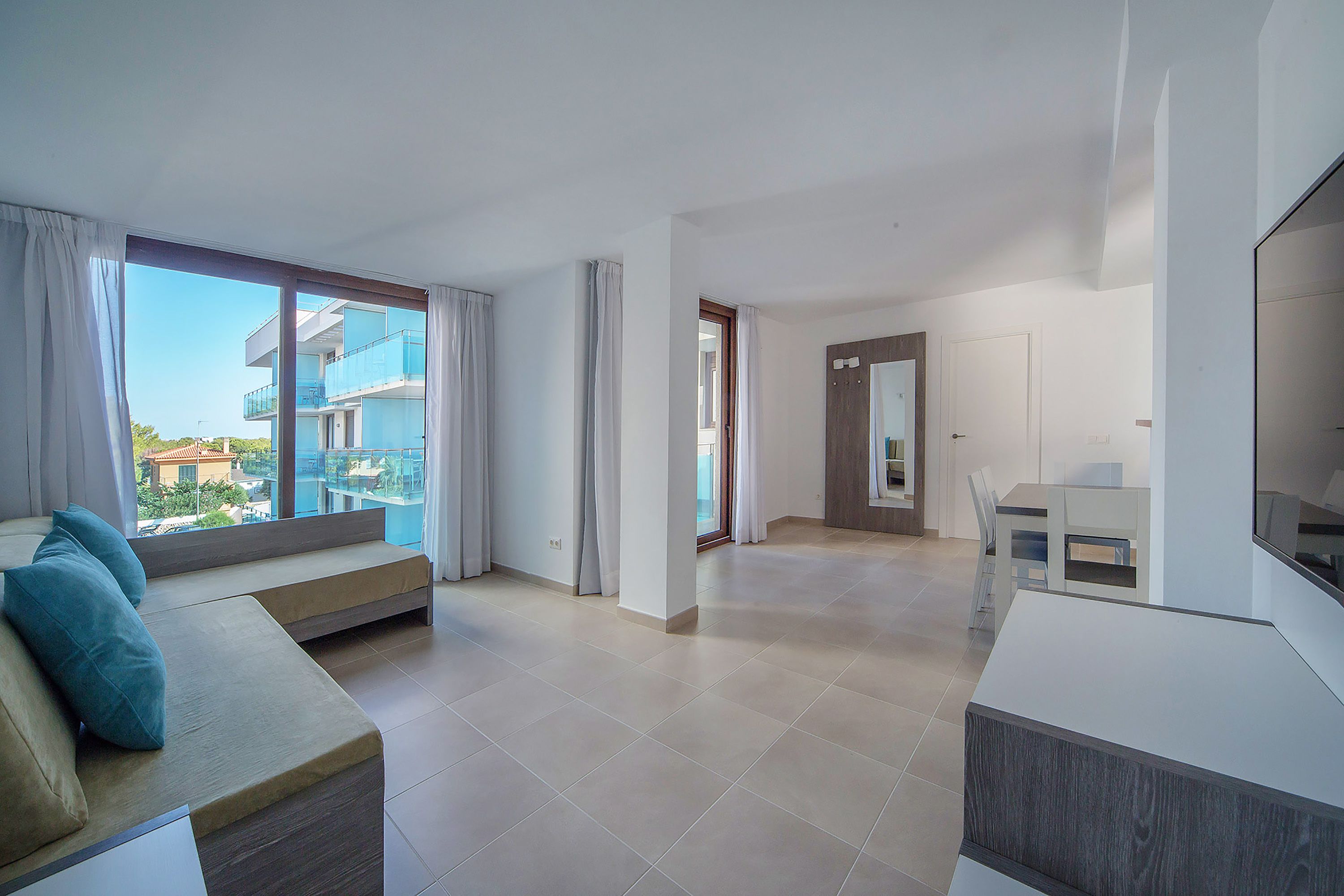 A modern apartment with a large balcony, a sofa, a dining area, and a TV.