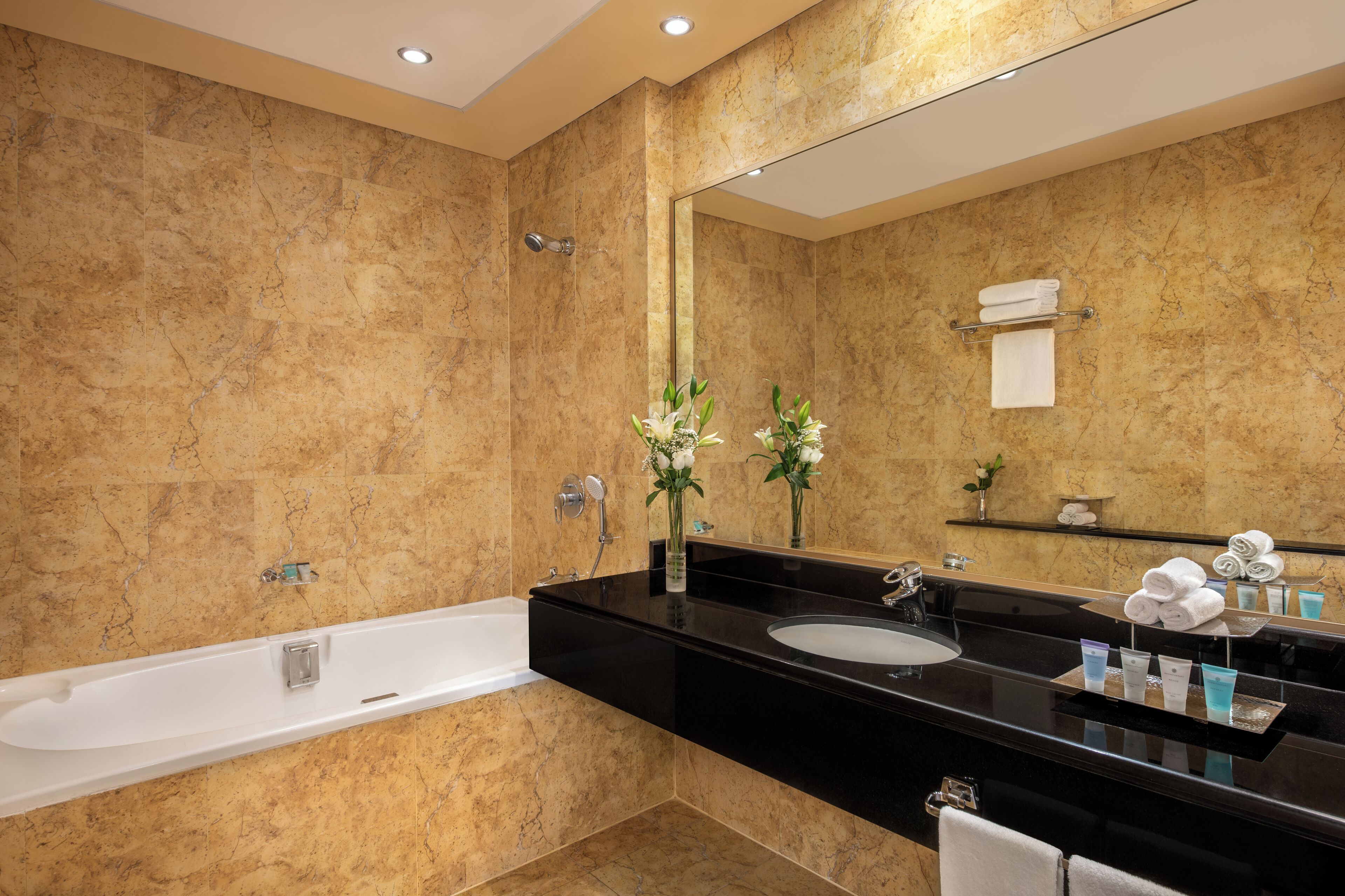 A modern bathroom with a marble wall, a black sink, a large mirror, and a bathtub.
