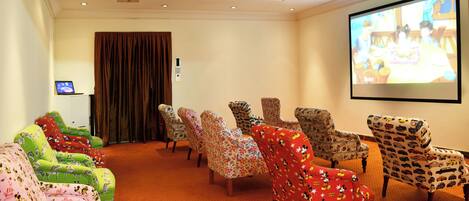 A conference room with multiple rows of chairs, a projector screen, and a television.