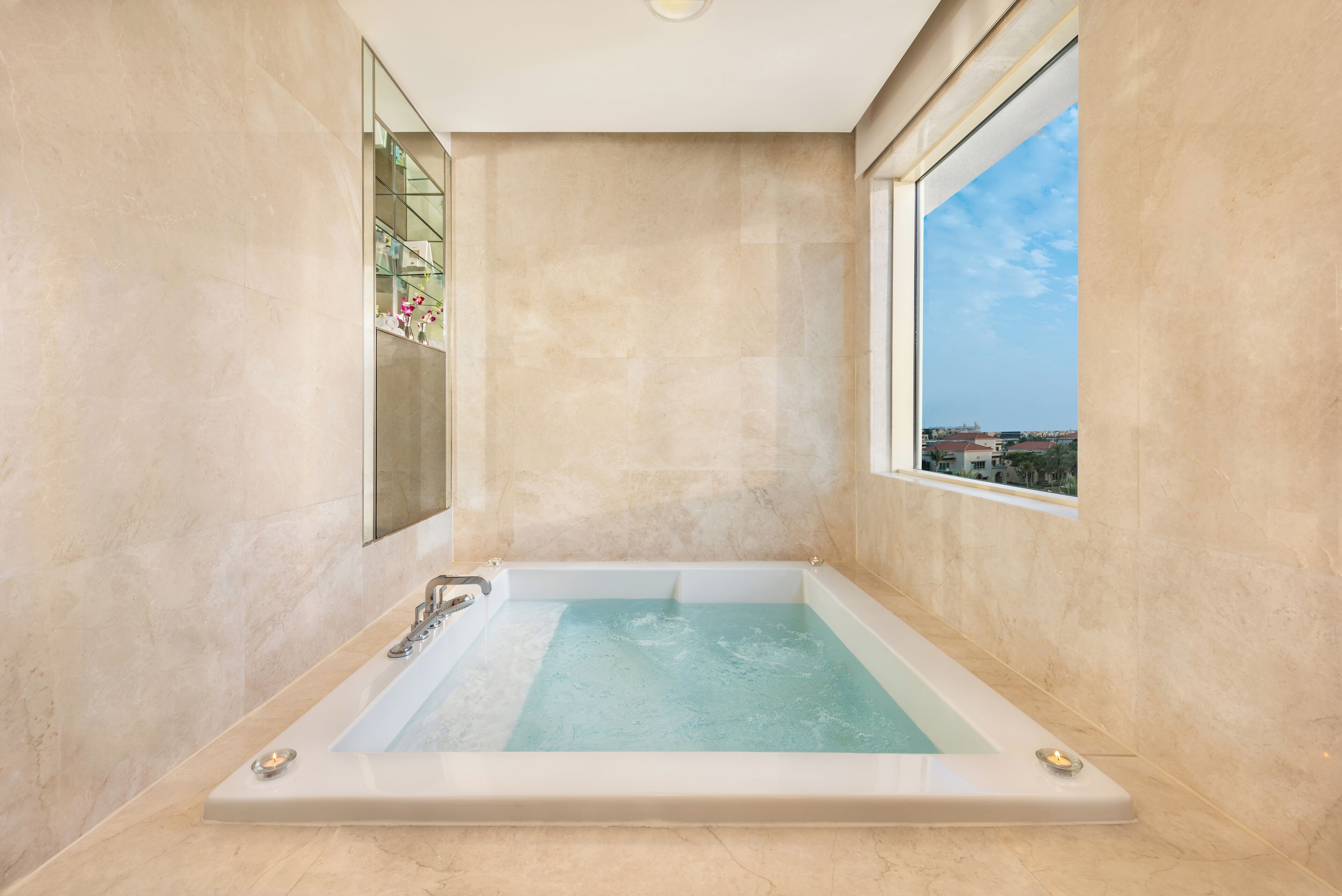 Une salle de bain spacieuse avec une grande baignoire, une fenêtre donnant sur la ville et des murs en marbre.