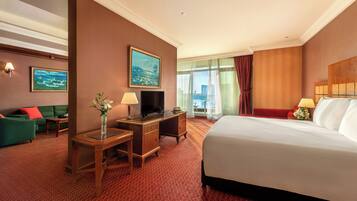 A hotel room with a large bed, a desk with a TV, a sofa, and a view of the city.