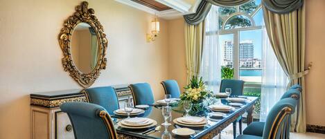 A dining room with a long table set for six, blue upholstered chairs, a large ornate mirror, and a chandelier.
