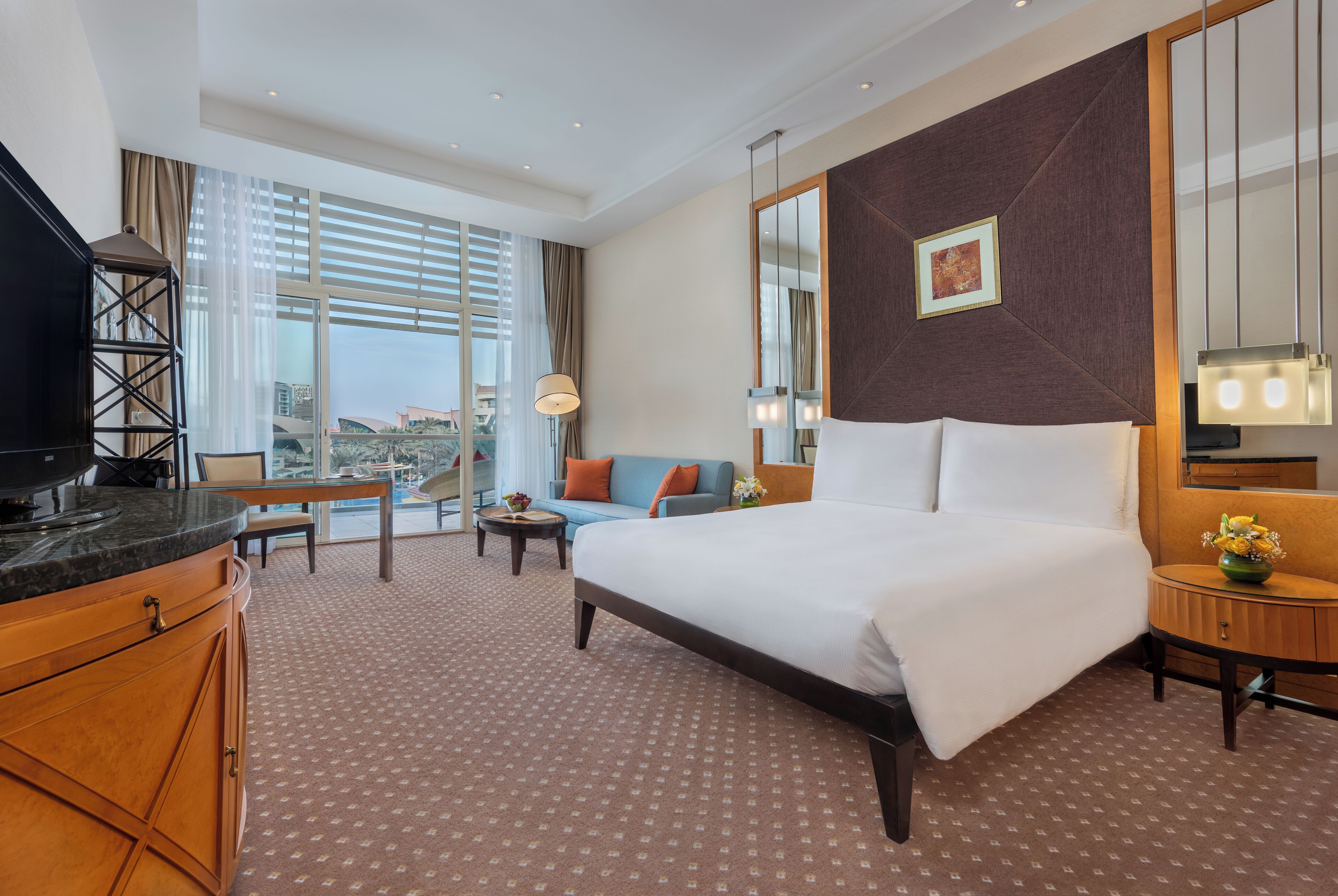 A hotel room with a large bed, a sofa, a desk, and a TV.