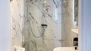 A modern bathroom with marble walls, a glass-enclosed shower, a white sink, and a toilet with a towel.