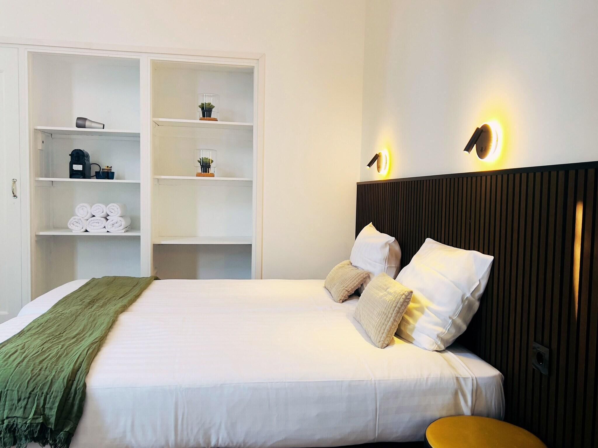 A hotel room with a bed, a wardrobe with shelves, and a bedside table.