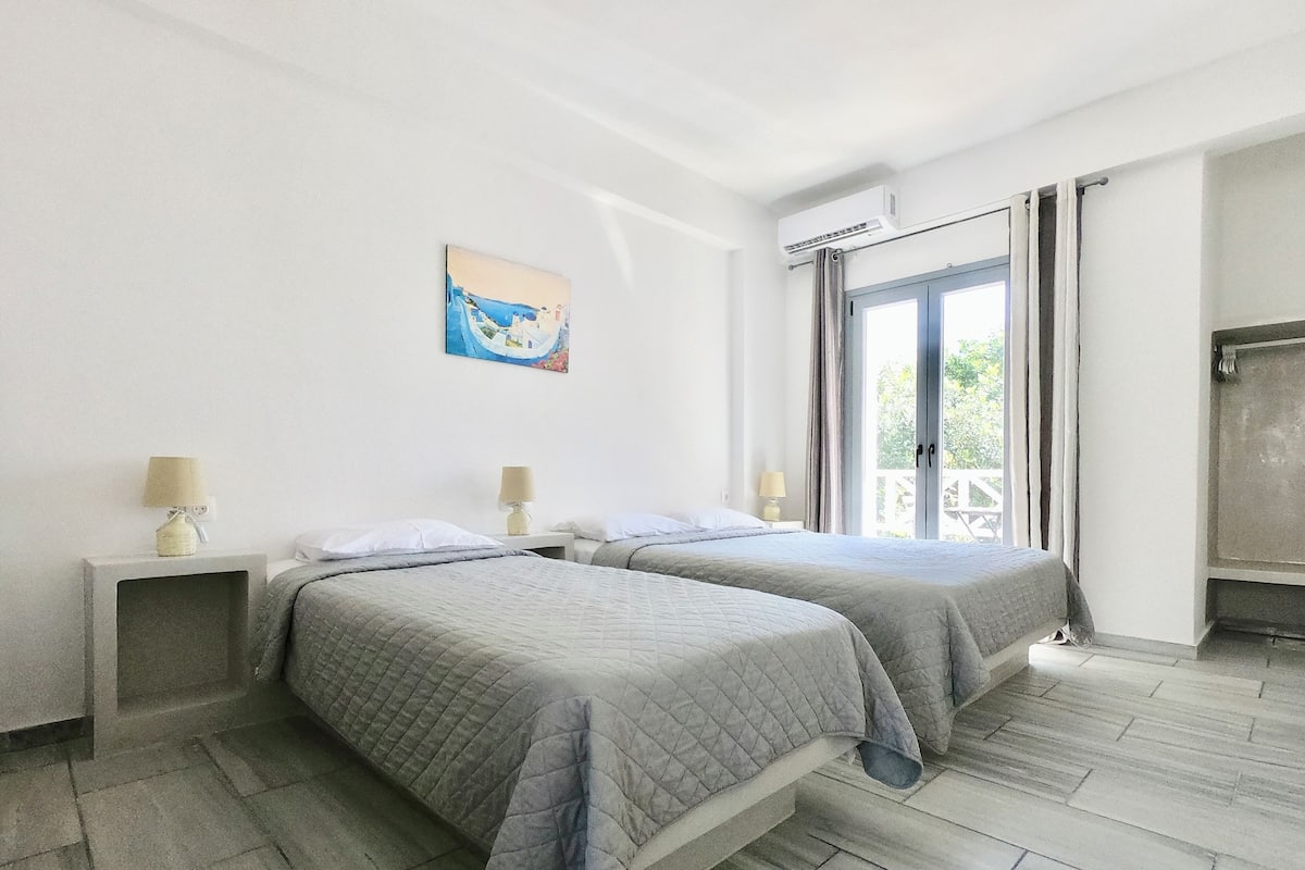 Habitación de hotel con dos camas, un cuadro en la pared, un equipo de aire acondicionado y vistas a través de un ventanal grande.