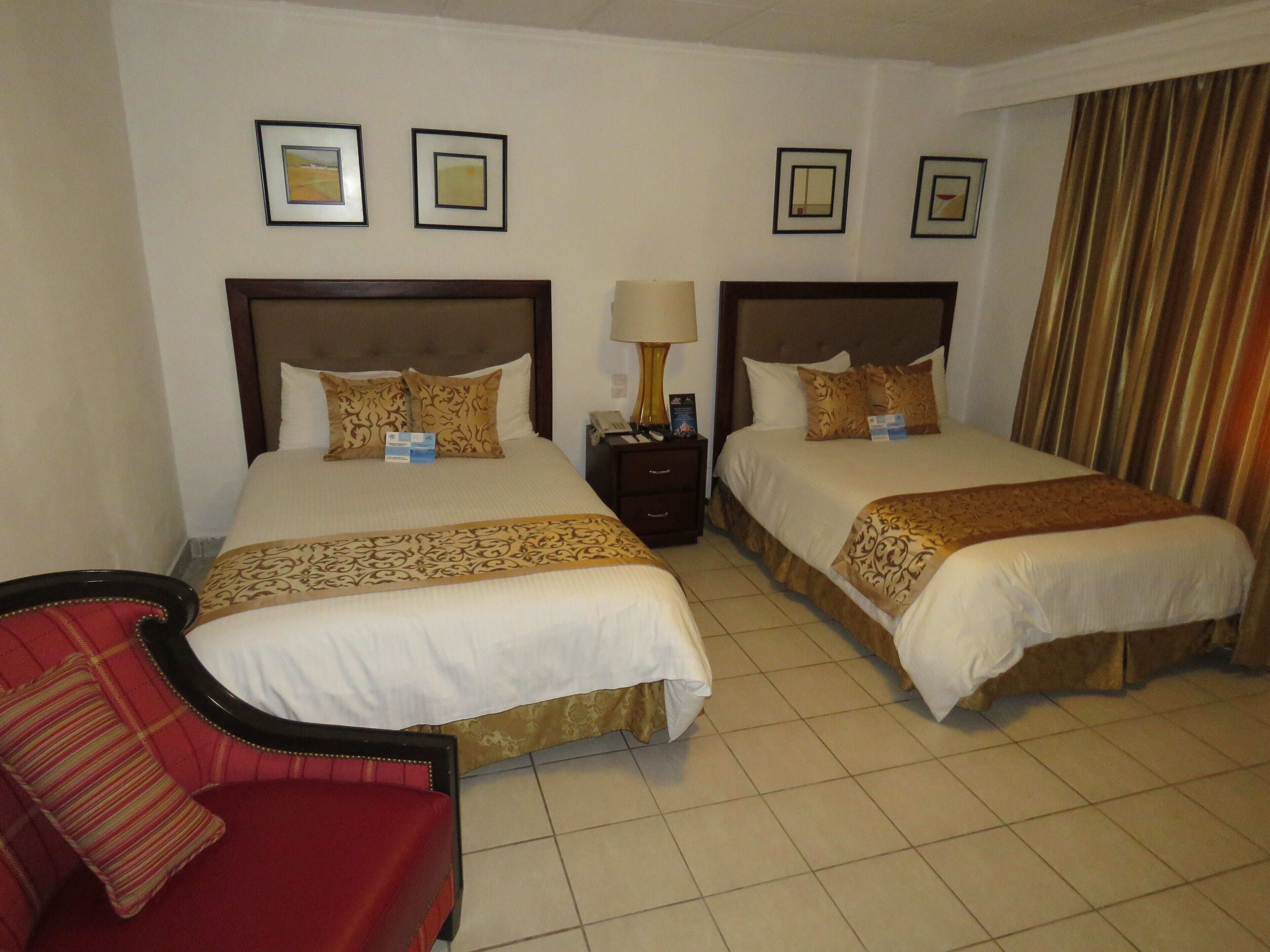 A hotel room with two beds, a nightstand, a lamp, and a red chair.