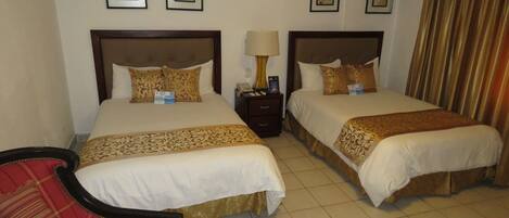 A hotel room with two beds, a nightstand, a lamp, and a red chair.