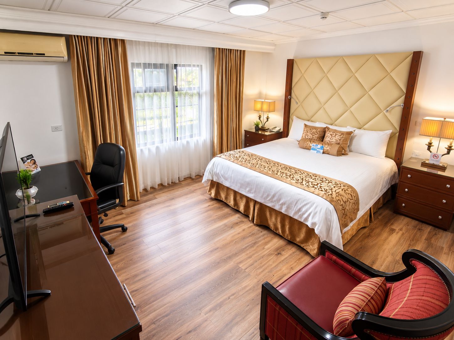 A hotel room with a bed, bedside tables, a desk with a chair, a TV, and a window with curtains.