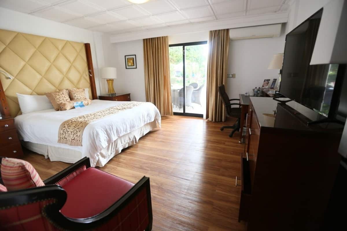 Habitación de hotel con una cama grande, un escritorio con televisor, una silla y un ventanal corredizo al exterior.