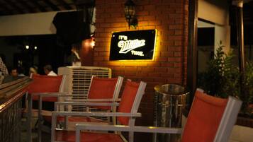 Um restaurante com uma placa de neon que diz "It's Villa's Time". Há várias cadeiras de metal com almofadas laranja e uma parede de tijolos ao fundo.