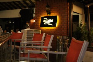 Un restaurante con un letrero de neón que dice "It's Villa's Time". Hay varias sillas de metal con cojines naranja y una pared de ladrillo al fondo.
