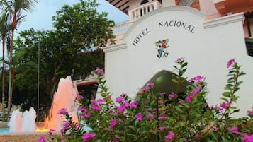 Entrada de hotel con una fuente y abundante vegetación.