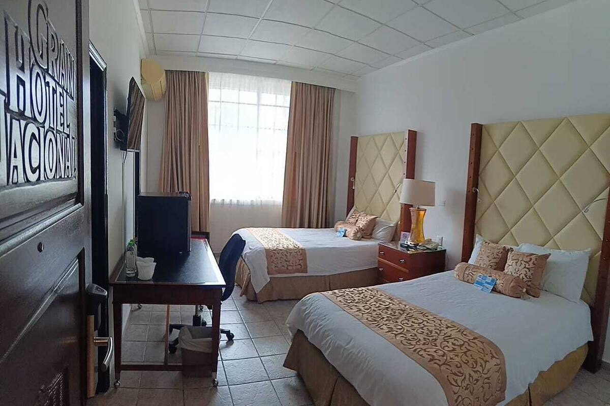 Habitación de hotel con dos camas, un escritorio, un televisor y una ventana con cortinas.