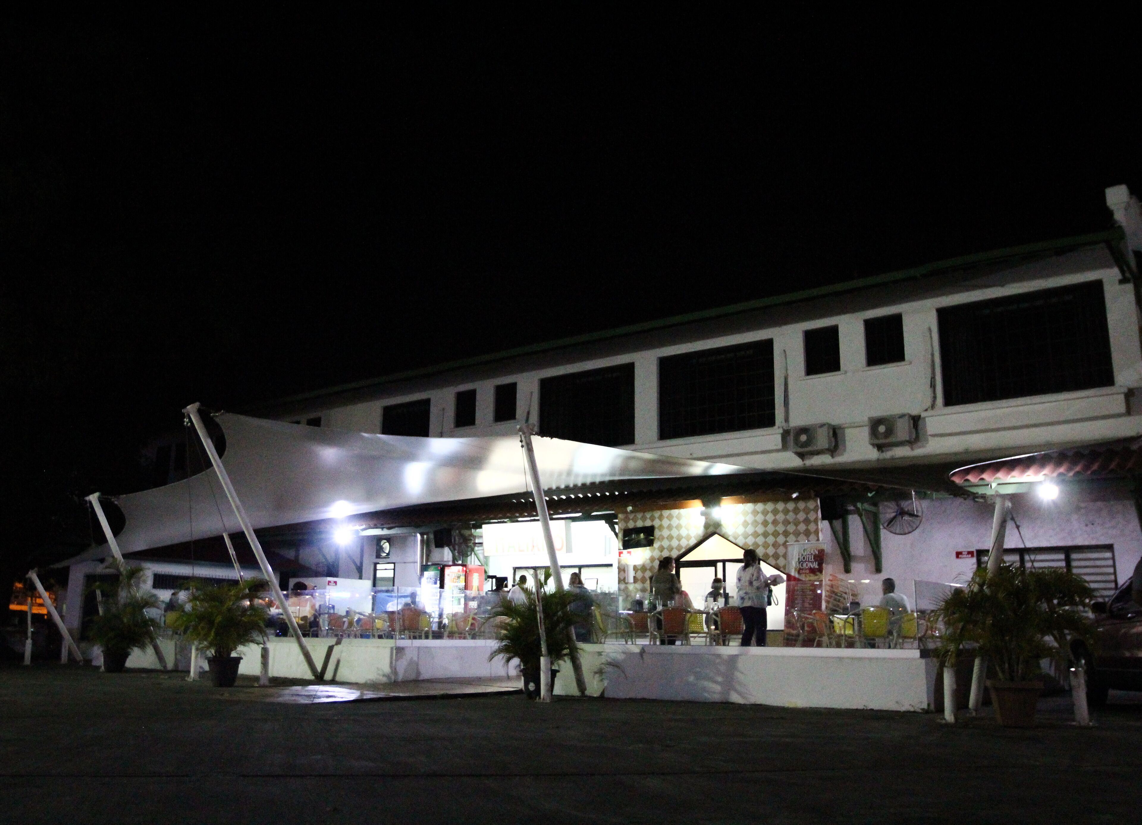 A hotel with a covered outdoor seating area, multiple air conditioning units, and a sign indicating it is a hotel.
