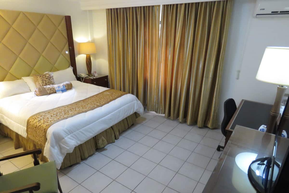 Habitación de hotel con una cama grande, un escritorio, una silla, una lámpara y cortinas.