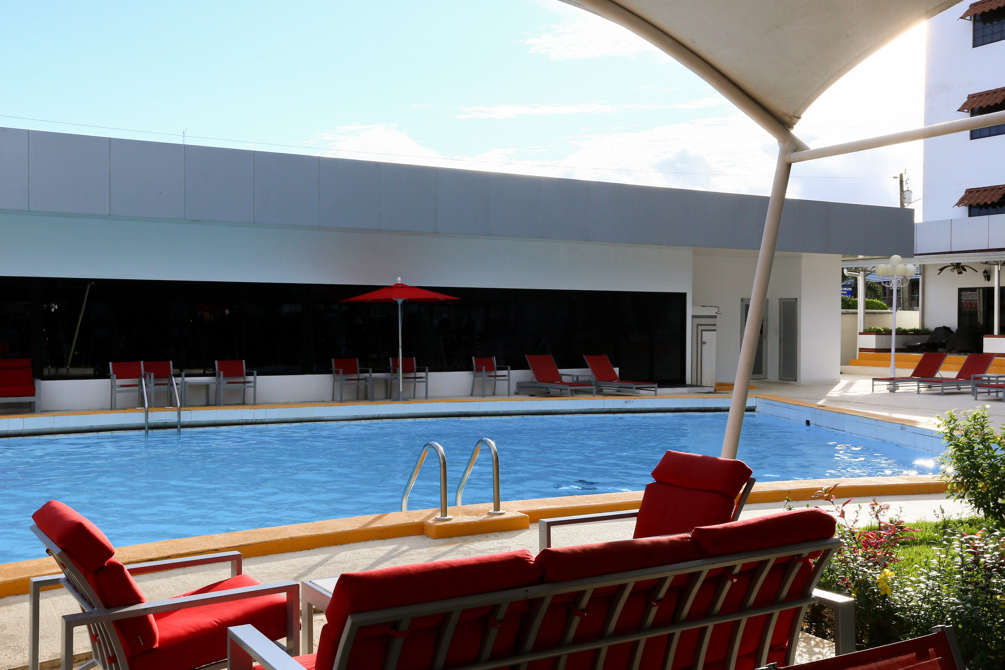 Una piscina con sillas de descanso y una sombrilla rojas.