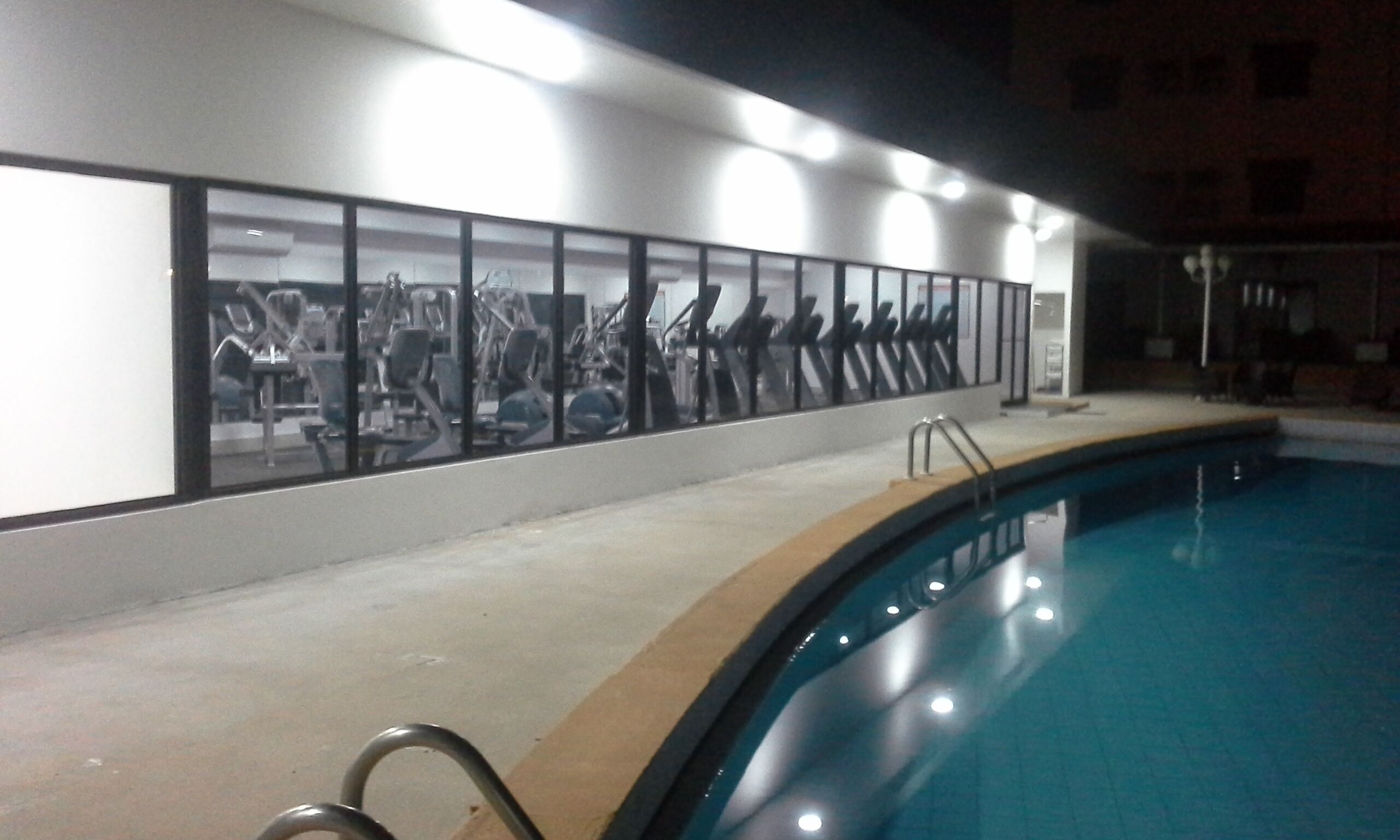A swimming pool with a glass wall reflecting gym equipment.