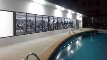 A swimming pool with a glass wall reflecting gym equipment.