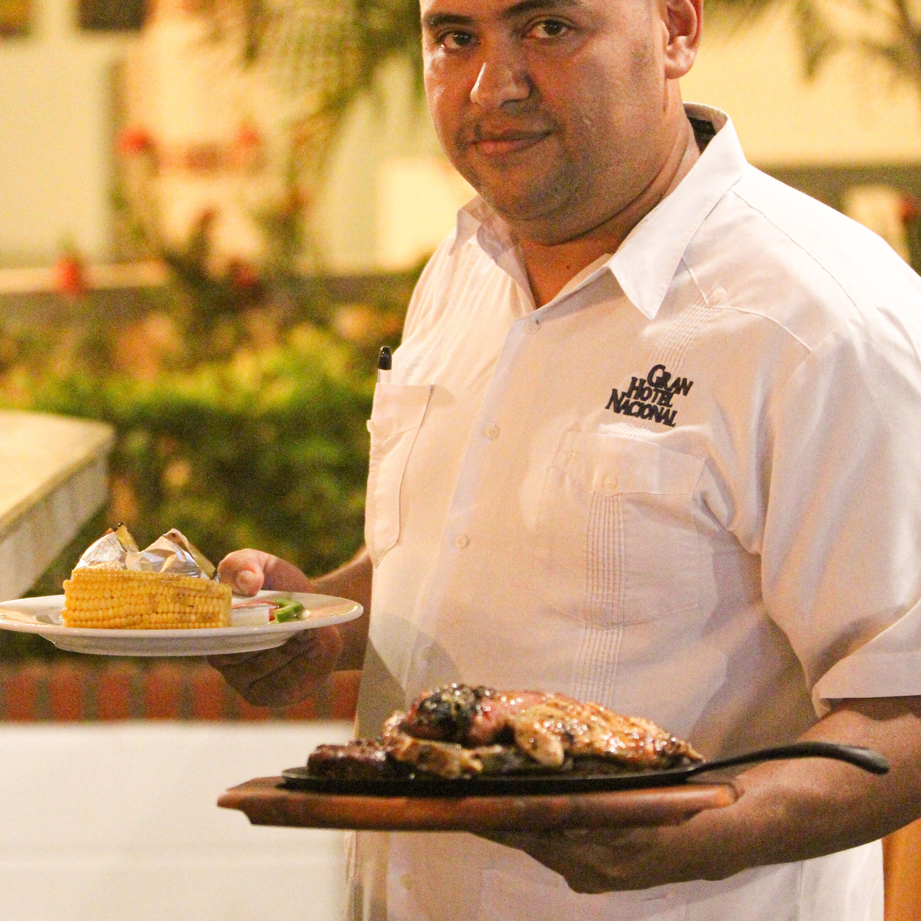 Una persona con camisa blanca sostiene un plato con postre y un plato de comida.