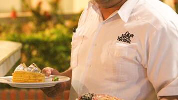 Una persona con camisa blanca sostiene un plato con postre y un plato de comida.