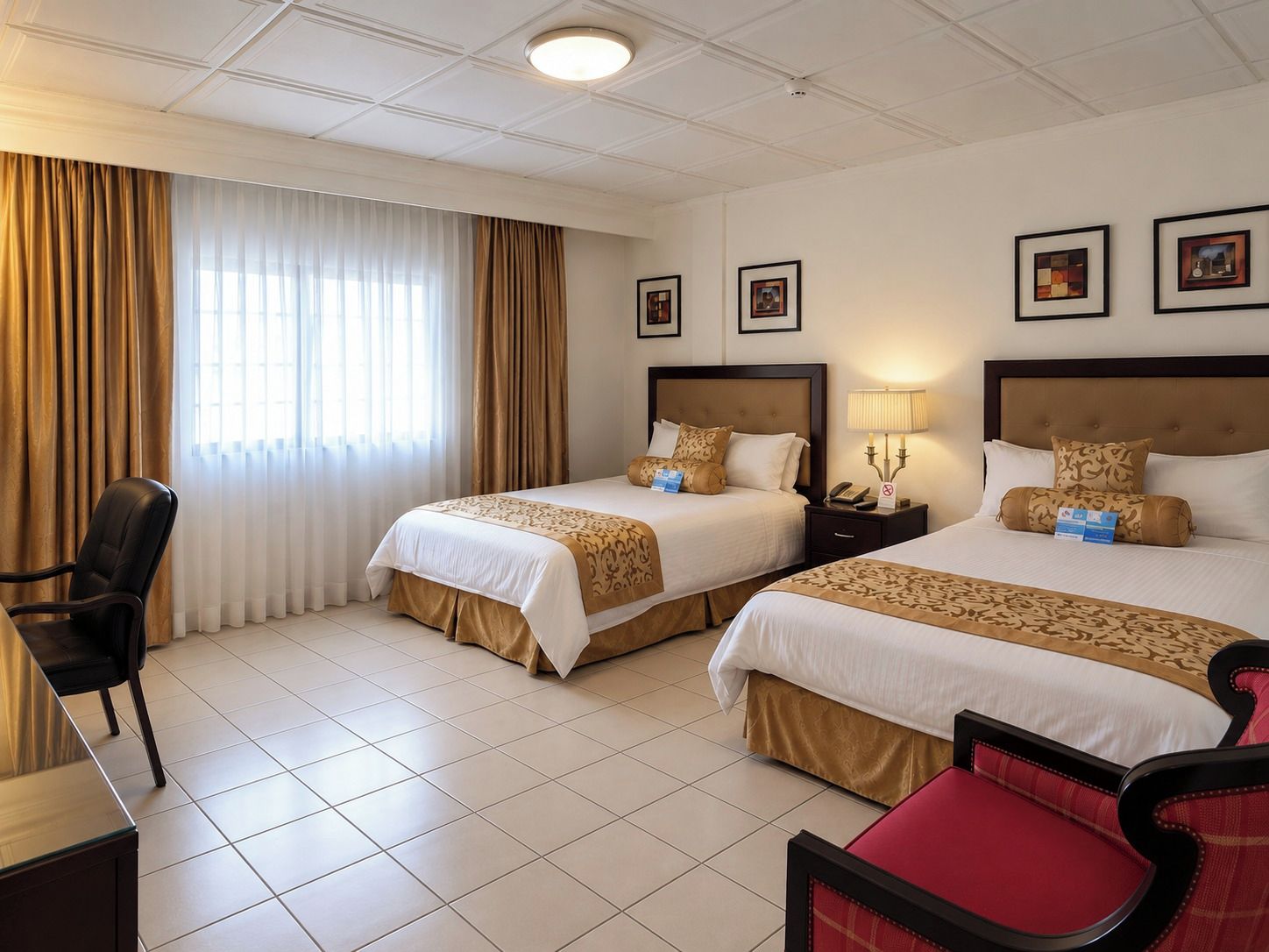 Habitación de hotel con dos camas, un escritorio, una silla y una ventana con cortinas.