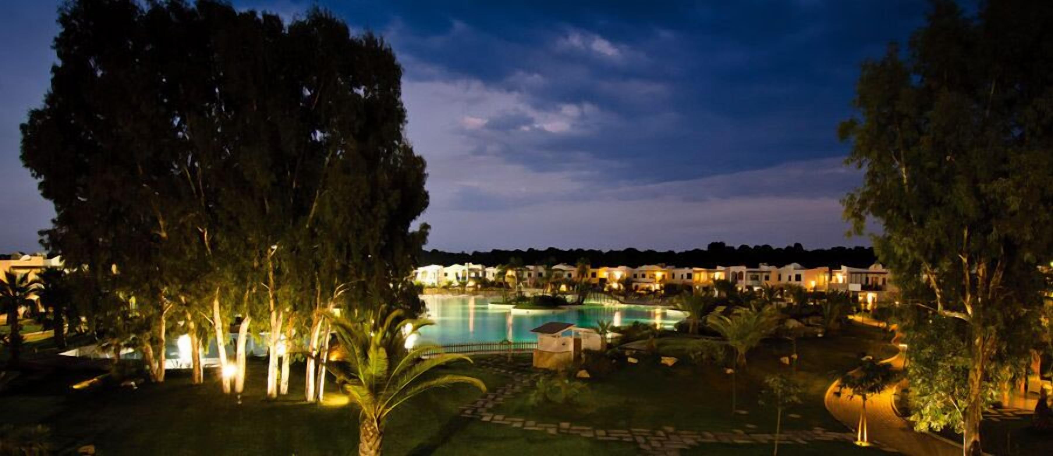 Un resort con piscina, palmeras y edificios iluminados durante la noche.