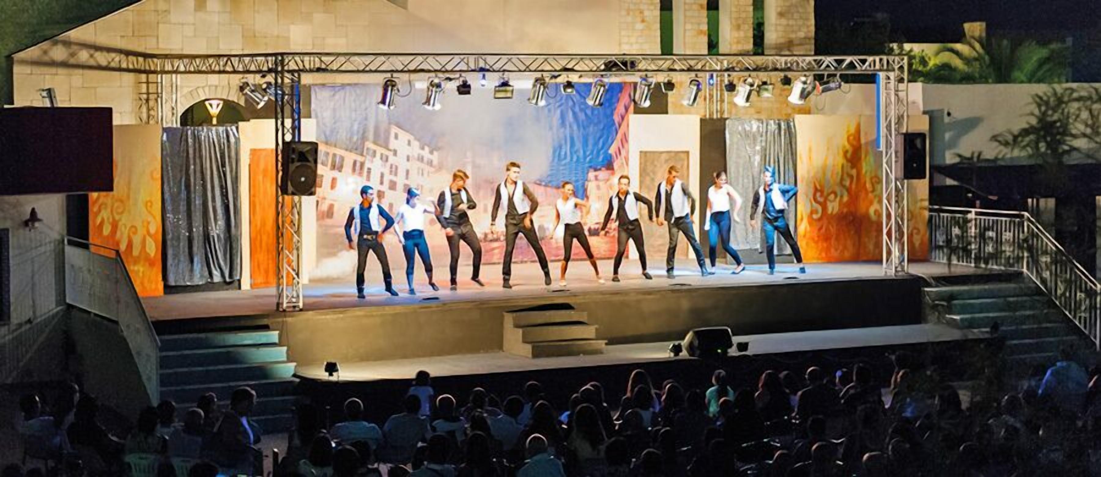 Un escenario con un grupo de bailarines actuando frente a un telón que muestra un paisaje urbano.
