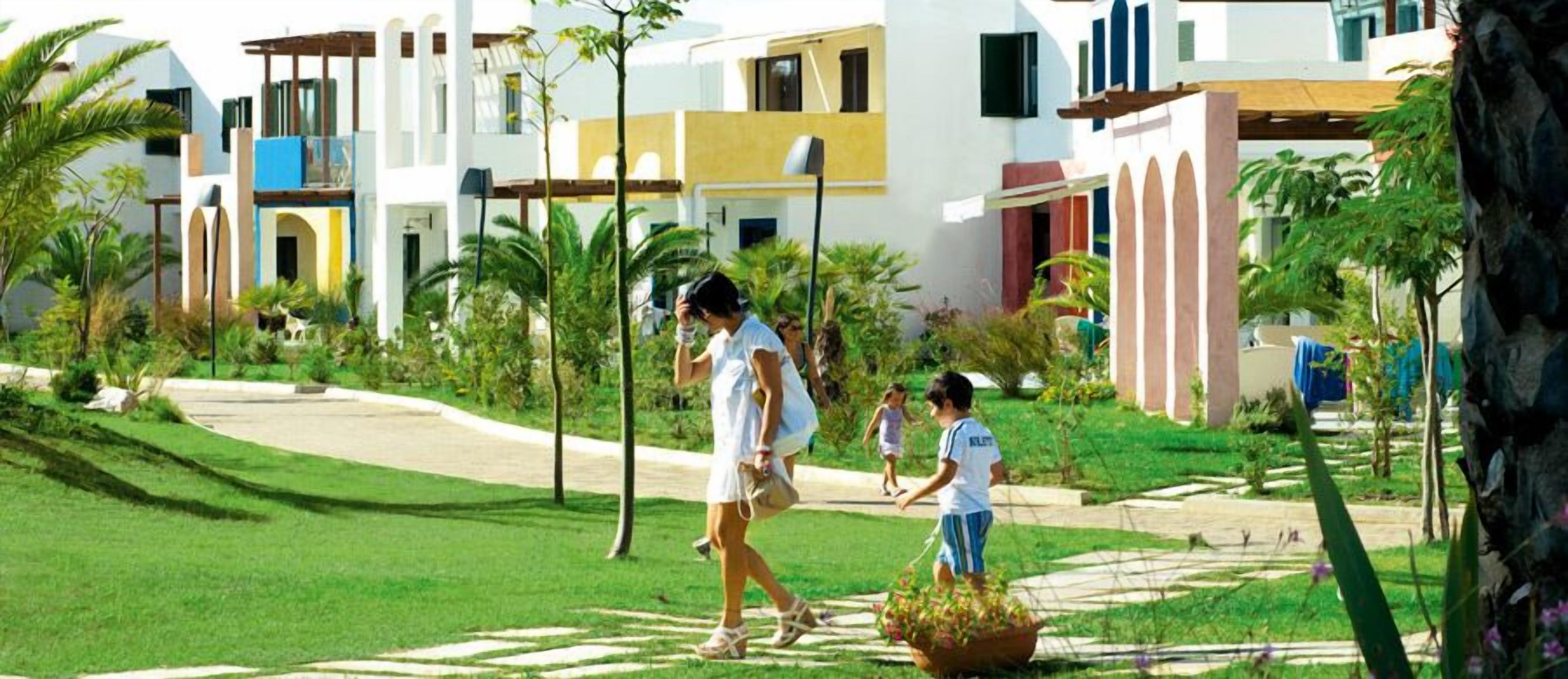 Un complexe hôtelier doté d’une promenade dallée, de palmiers et de bâtiments modernes avec balcons.