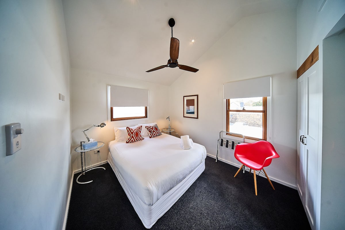 Ein Hotelzimmer mit einem großen Bett, einem Deckenventilator, einem roten Sessel und einem Fenster mit Blick.
