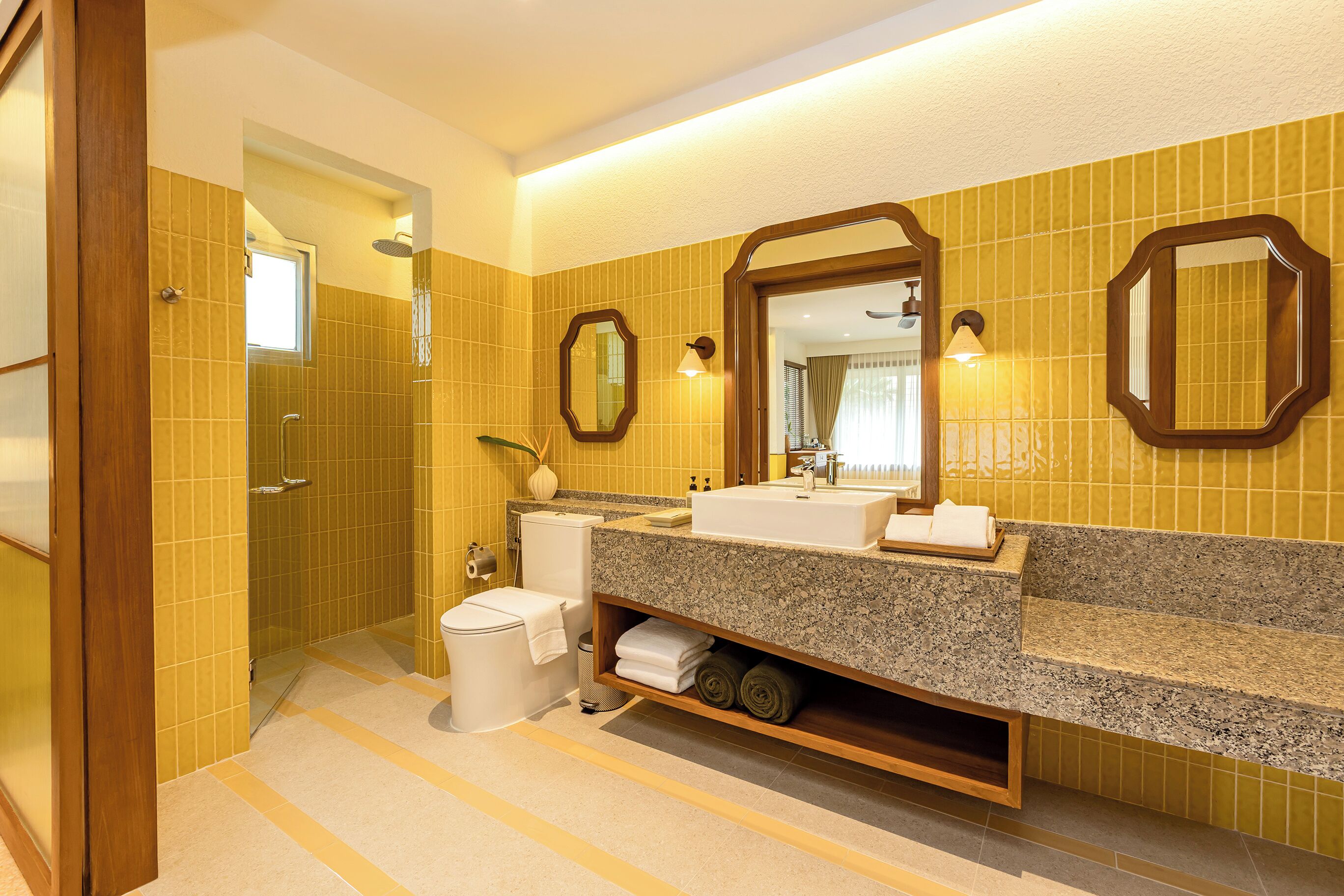 A hotel bathroom with a shower, toilet, sink, and large mirrors.