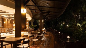 A restaurant with wooden tables and chairs, a bar area, and a covered outdoor seating area with plants. - Pakasai Resort (Krabi)