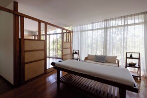 A traditional Japanese-style room with tatami flooring, a low wooden bed, a sofa with cushions, and a sliding shoji screen door.