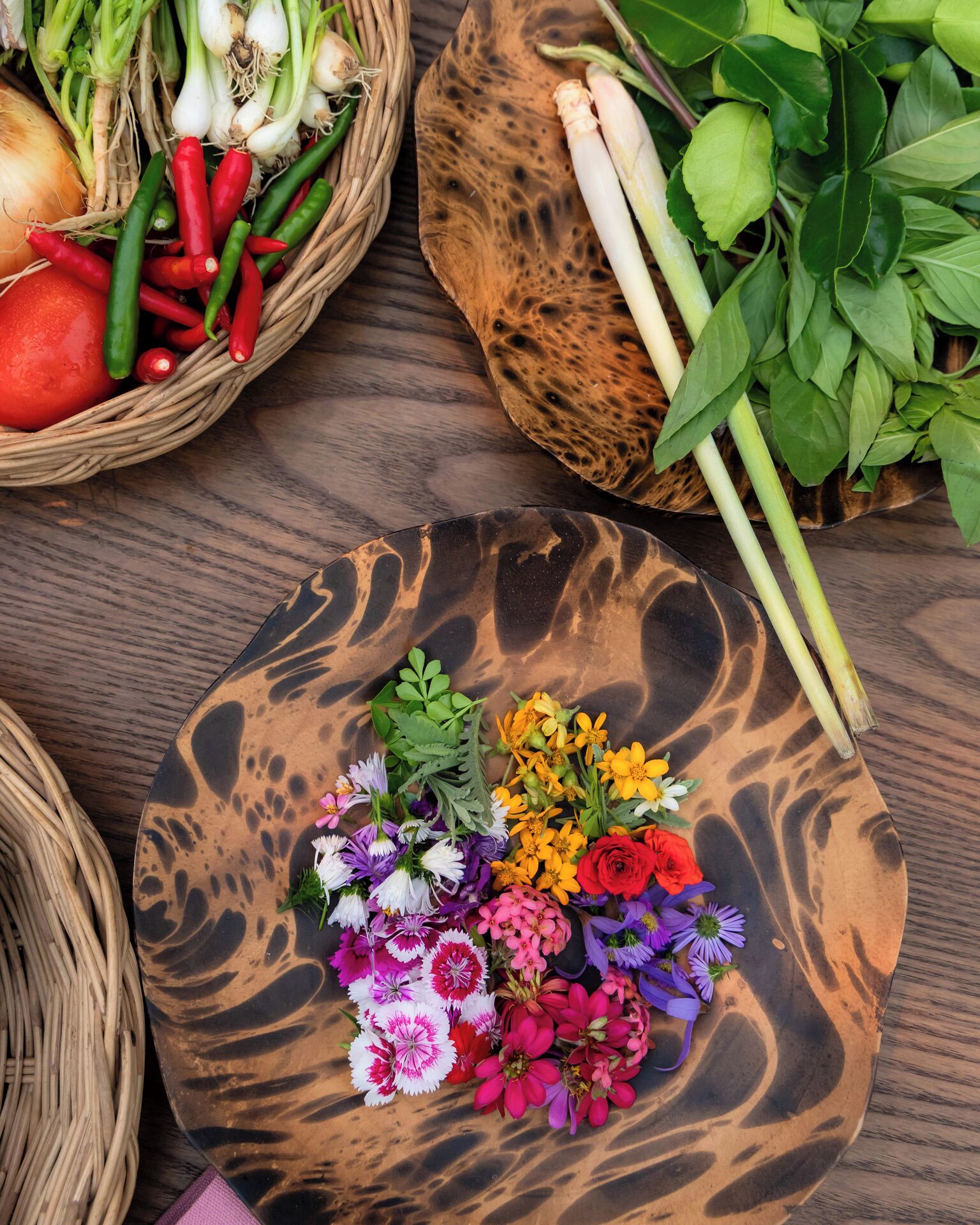 A wooden table with a variety of fresh vegetables and colorful flowers.