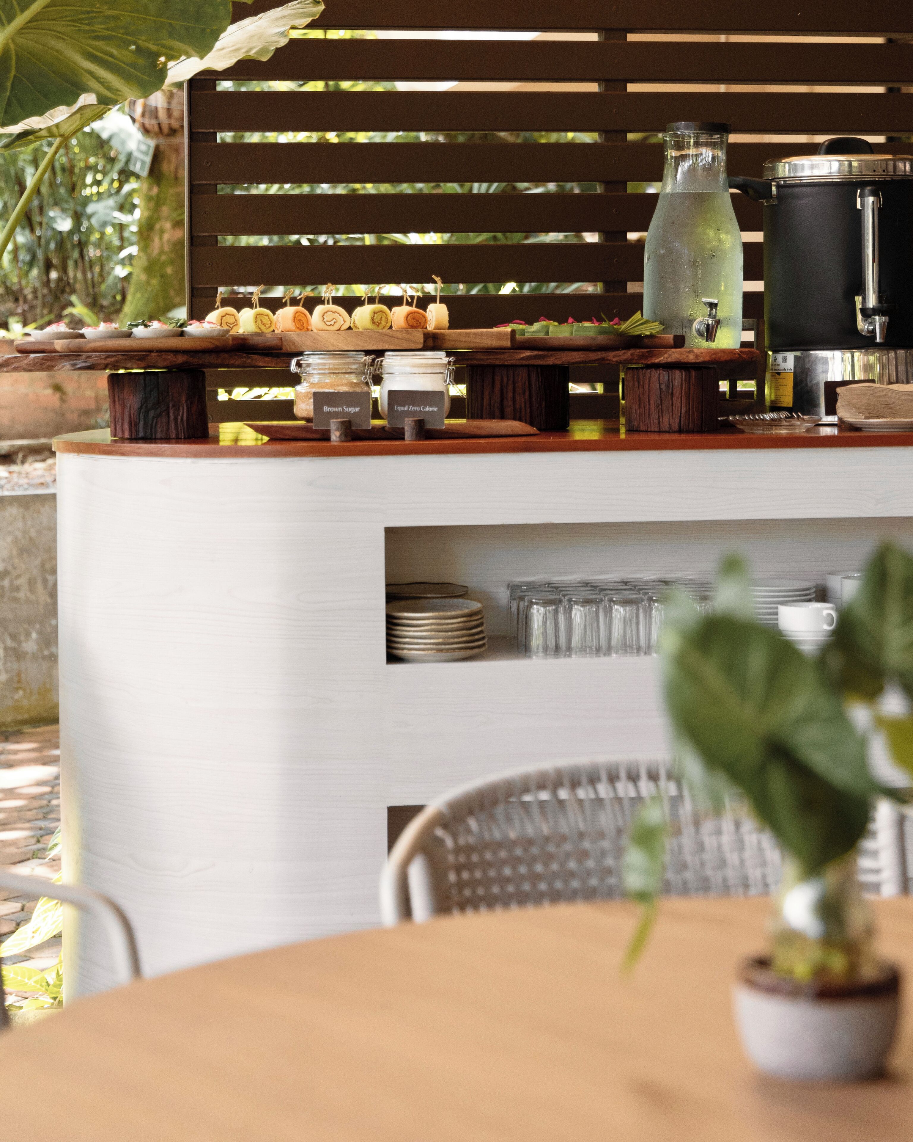 An outdoor bar area with a wooden slatted backdrop, a coffee maker, and jars labeled with ingredients.