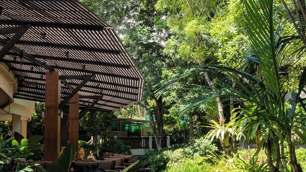 A covered outdoor area with tables and chairs, surrounded by lush greenery and a small pond. - Pakasai Resort (Krabi)