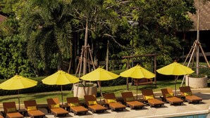 A poolside area with lounge chairs and yellow umbrellas, surrounded by lush greenery and a view of the ocean. - Pakasai Resort (Krabi)