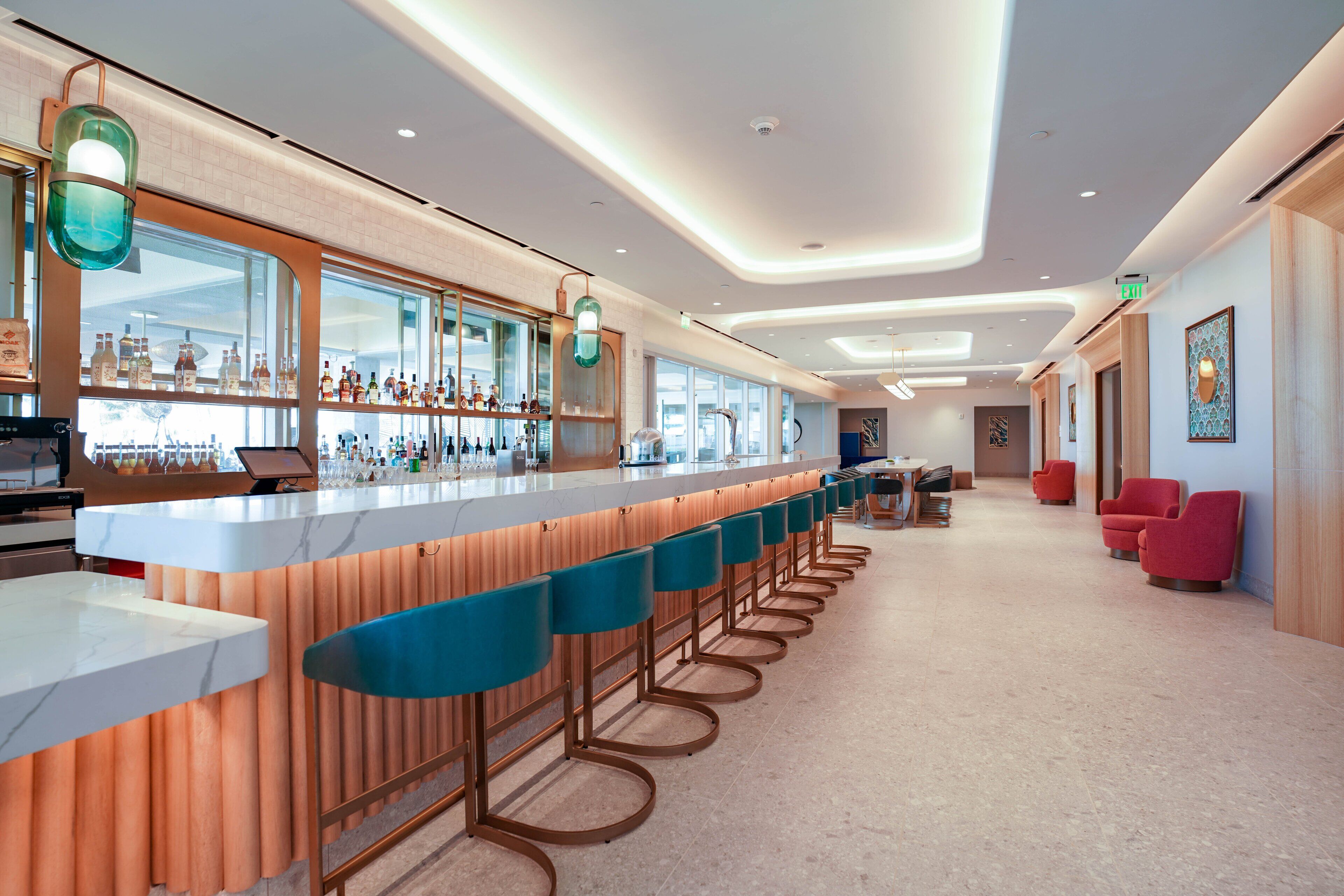 A modern bar area with a long counter, bar stools, and a variety of bottles.