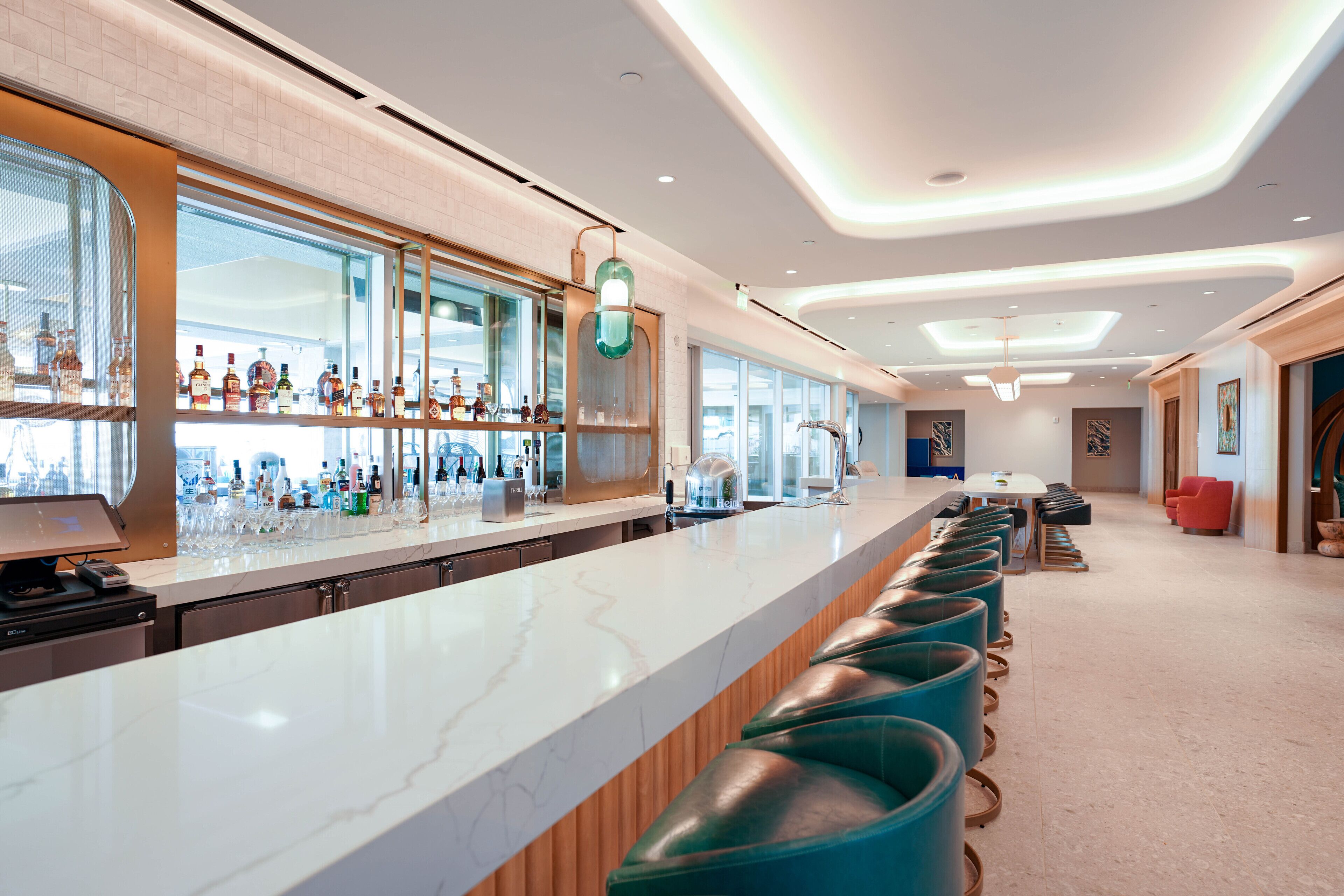 A modern bar area with a long counter, bar stools, and a variety of bottles.