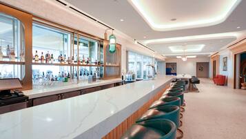 A modern bar area with a long counter, bar stools, and a variety of bottles.