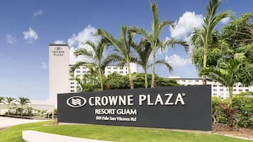 Naamplaatje voor Crowne Plaza Resort Guam, met een heldere lucht en palmbomen op de achtergrond.