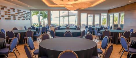 A conference room with multiple round tables and chairs, large windows, and a modern ceiling design.