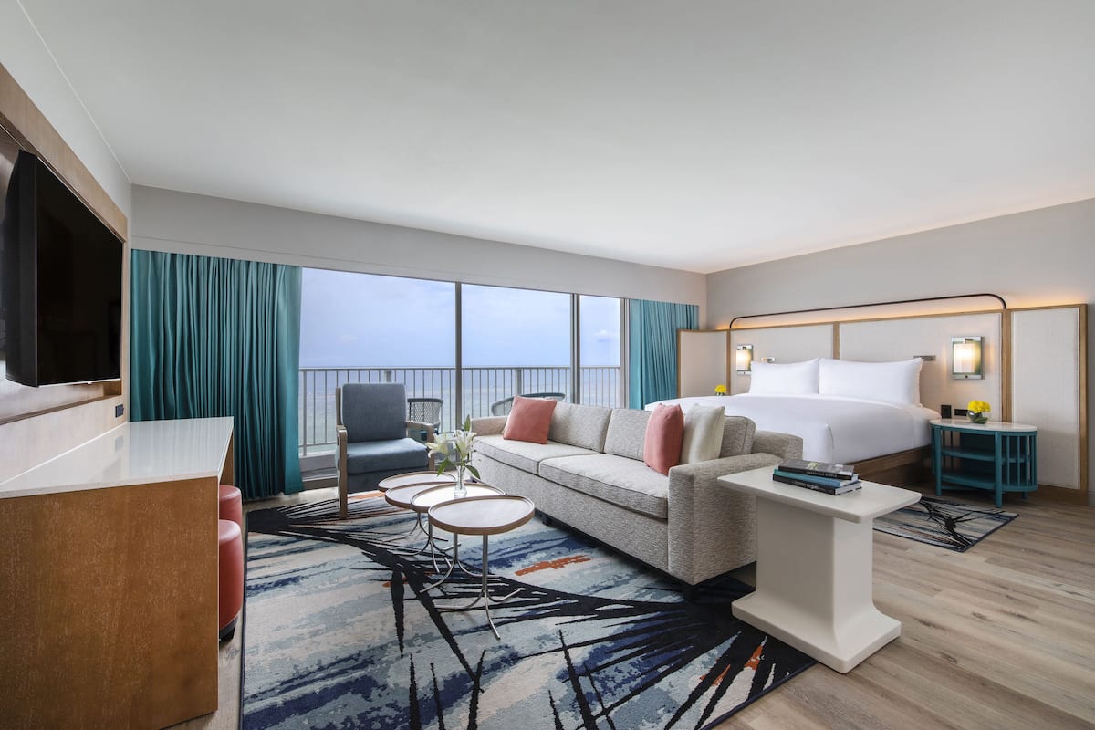 A modern hotel room with a large bed, a sofa, a coffee table, and a TV.