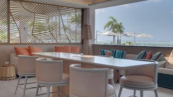 A modern outdoor seating area with a long table and bar stools, overlooking a beach.