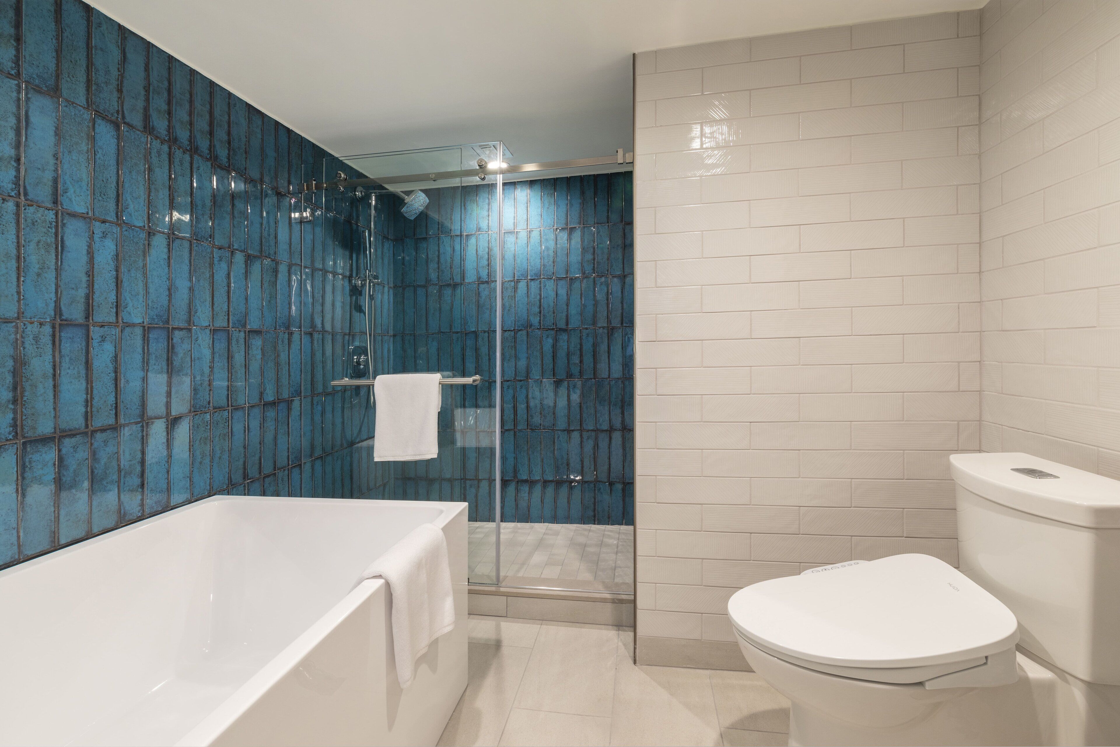 Un baño moderno con bañera, inodoro y zona de ducha con mampara de vidrio.