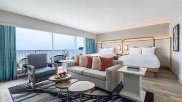A hotel room with a balcony, a bed, a sofa, a small table, and a chair.