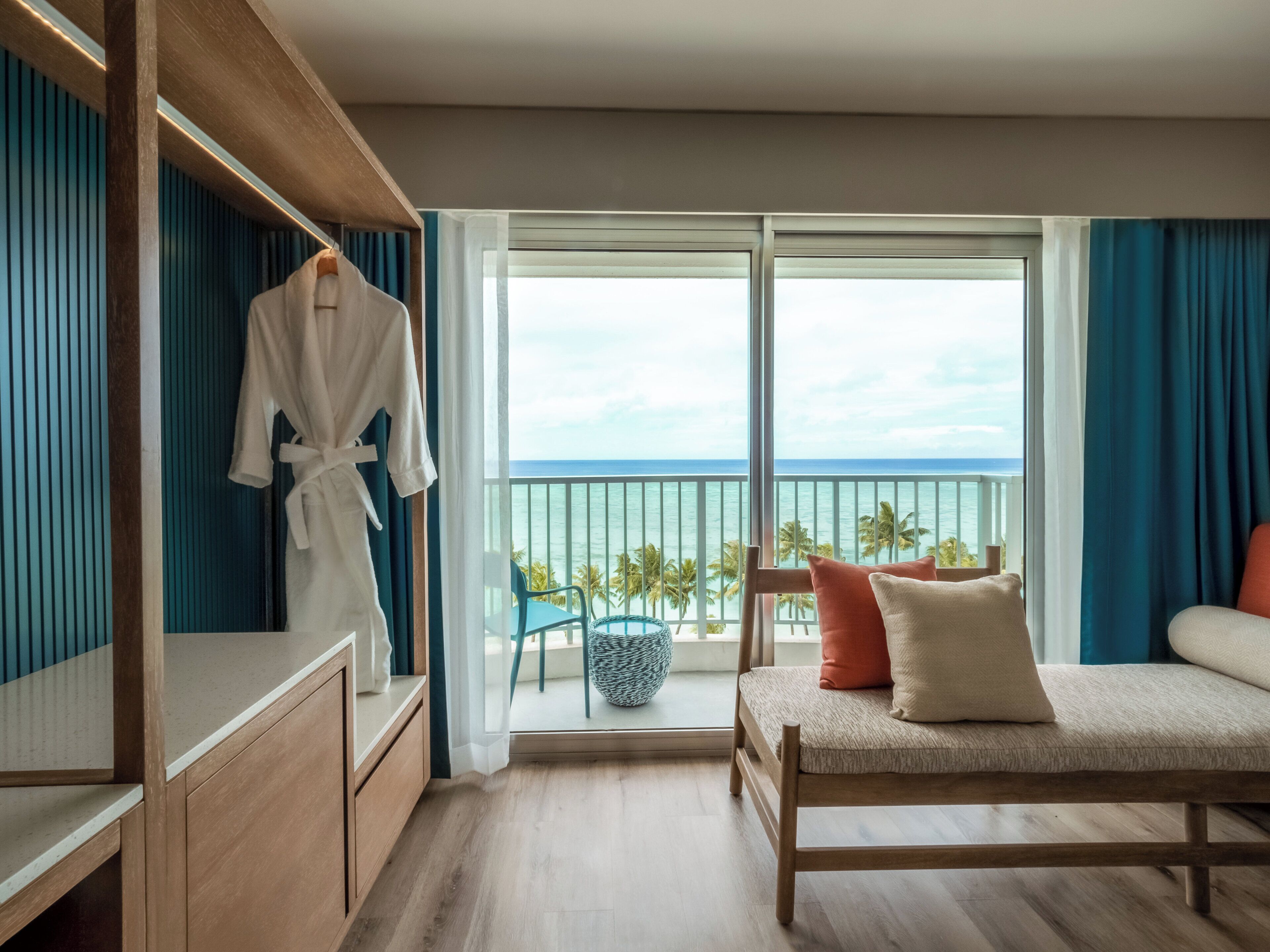 A hotel room with a balcony, a bed, a seating area, and a wardrobe.